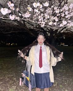 a woman standing under a tree with her hair blowing in the wind and wearing a tie