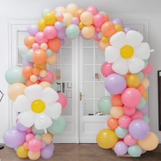 an arch made out of balloons with flowers on the top and bottom, is decorated in pastel colors