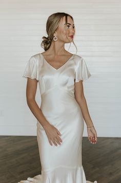 a woman in a white dress standing on a wooden floor with her hands behind her back