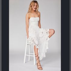 a woman in a white dress is sitting on a stool and posing for the camera