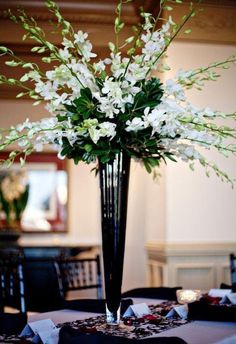 a tall black vase filled with white flowers on top of a round table covered in napkins