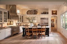 a large kitchen with white cabinets and wooden flooring, along with a dining table surrounded by chairs