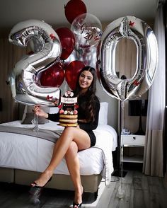 a woman sitting on top of a bed holding a cake in front of some balloons