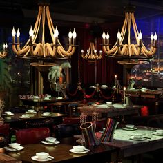 a dining room filled with lots of tables covered in white plates and place settings under chandeliers