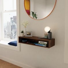 there is a mirror on the wall above a shelf with books and a lamp next to it