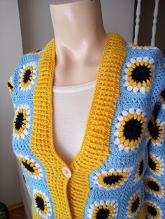 a yellow and blue crocheted sweater with sunflowers on it, sitting on a mannequin