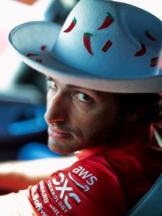 a man wearing a white hat with chili peppers on it's brim and sitting in a car