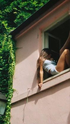 a woman leaning out the window of a pink building with ivy growing on it's side