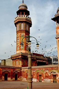 birds flying around an old building in the middle of town, with two tall towers on each side