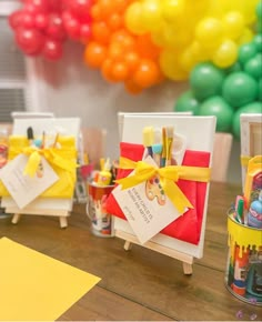 there are many items on the table with yellow ribbon around them and some balloons in the background