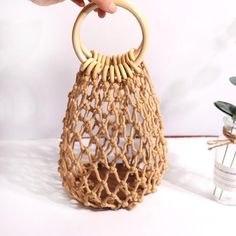 a hand holding a wooden handle on top of a woven bag next to a potted plant