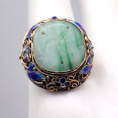 Vintage Chinese silver ring in floral filigree designs with vermeil finish and colorful enamel decorations, featuring carved oval green Jade centerpiece. The size is adjustable. This gorgeous ring is a size 7 1/4 (adjustable), 24 mm at the widest and weighs 6.5 grams. It features some enamel loss. EA2362 Ornate Oval Enamel Jewelry, Green Enamel Jewelry For Wedding, Green Enamel Wedding Jewelry, Green Oval Enamel Ring For Formal Occasions, Formal Green Oval Enamel Ring, Formal Oval Green Enamel Ring, Green Enamel Ring For Wedding, Green Enamel Wedding Ring, Oval Green Enamel Ring Gift