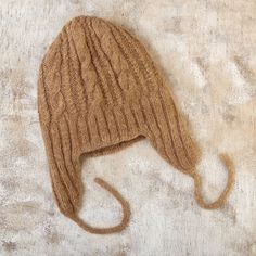 a brown knitted hat laying on top of a wooden floor next to a white wall