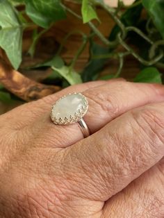 This cool, white Rainbow Moonstone gemstone ring reminds me of the puffy clouds that accent a Spring day. After a rain you can see the dark clouds turn to wisps of white with a faint rainbow glistening through. This stone is just that! As you look at the ring and turn it you will see subtle flashes of blue purple and maybe green. The lovely way the stone is nestled within the Sterling silver scalloped bezel setting gives this special piece a dainty yet bold look and feel. Designed in a timeless White Natural Stones Promise Ring, White Natural Stone Promise Ring, Minimalist Handmade White Moonstone Ring, Unique White Adjustable Moonstone Ring, White Moonstone Opal Ring In Oval Cabochon Shape, Unique Adjustable White Moonstone Ring, Large Oval White Moonstone Ring, White Oval Moonstone Ring With Large Stone, White Crystal Birthstone Ring With Round Stone