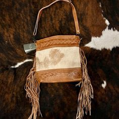 "Myra Bag Genuine Hand-Tooled Leather and Hairon Cowhide Bag 2616-09 Genuine Leather and Hairon Cowhide Bag 13\" x 12\" x 3.5\" deep 22\" Adjustable leather strap PLEASE NOTE: Although your bag will be the same style/design as in the picture, each handbag is one-of-kind. Every bag has a new unique piece of hide with slightly different pattern." Beige Fringed Hobo Bag For Daily Use, Beige Fringe Hobo Bag For Daily Use, Leather Bucket Bag With Tassels For Travel, Beige Fringed Hobo Tote Bag, Beige Fringe Bucket Bag For Everyday Use, Everyday Beige Bucket Bag With Fringe, Leather Fringe Bucket Tote Bag, Beige Leather Bags With Fringe, Everyday Fringe Bucket Bag