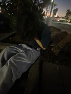 a person laying down on the sidewalk with their head in his hands, at night