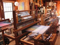 an old fashioned weaving machine in a room with lots of books on the shelves and windows