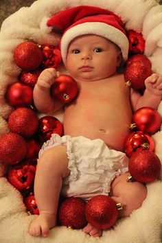 a baby wearing a santa hat surrounded by christmas ornaments