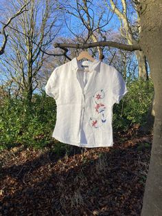 Hand embroidered linen shirt. Beautiful white t-shirt blouse with blue and pink floral embroidery pattern.  This is an upcycled item. Original brand: Mark O'Polo Labelled EU size 40 Item is in very good condition, however there is some very minor colouration on the inside of the collar. This is due to the second-hand nature of this item. NOTICE Please note that all my items are either second hand or vintage items which I upcycle. Due to the nature of the items being second hand/vintage, there may be nature signs of wear in them. However, I will always point out any noticeable flaws in my description. All items are hand designed and embroidered making each piece unique. I want to encourage people to breathe new life into second hand items so that they don't just get thrown away. Instead, we Outfits With Collared Shirts, Embroidered Linen Shirt, Floral Embroidered Shirt, Brand Mark, Floral Embroidery Patterns, Hand Embroidery Flowers, Embroidery Top, Embroidered Linen, Linen Blouse