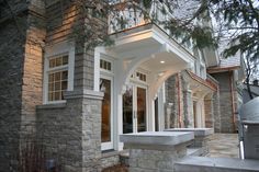 the front entrance to a house with stone steps and columns on both sides, surrounded by pine trees