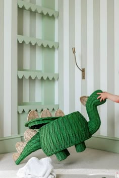 a child playing with a green toy alligator in a room that has striped walls and shelving