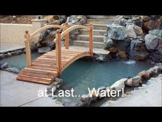 a wooden bridge over a small pond with rocks and water flowing from it to the ground