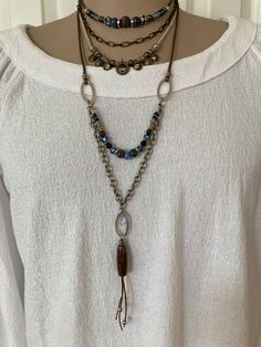 1mm strands of bronze leather with delicate silver beads dangle from a glossy natural agate in shades of brown. 3 upcycled silver tapered ovals are featured in this 2 strand statement necklace of silver chain and an intriguing gathering of glass and stone beads in rich blues and browns. Adjustable Beaded Metal Layered Necklace, Adjustable Metal Layered Necklace With Beaded Chain, Adjustable Double Strand Metal Necklace, Bohemian Silver Lariat Necklace With Natural Stones, Silver Bohemian Lariat Necklace With Natural Stones, Silver Beaded Dangle Necklaces, Bohemian Double Strand Necklace With Dangling Beads, Bohemian Silver Lariat Necklace With Beaded Chain, Adjustable Silver Bohemian Long Necklace