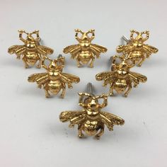 six gold bee pins with small faces on them