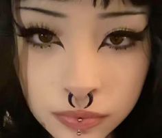 a close up of a woman with fake eyelashes and piercings on her nose, looking at the camera