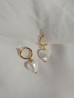 These dainty earrings are made with freshwater shell heart pearls and gold or platinum plated huggie hoops. This plating protects against wear and tear, tarnishing, and light contact with substances such as water. Closures: * Pierced gold hoops are hypoallergenic and nickel free (18 karat gold plated). * Pierced silver hoops are hypoallergenic and nickel free (platinum plated). * Clip on gold hoops are hypoallergenic and nickel free (18 karat gold plated). * Clip on silver hoops are hypoallergen Dainty Huggie Earrings With Pearl Charm As Gift, Dainty Pearl Charm Huggie Earrings As Gift, Dainty Pearl Charm Huggie Earrings For Gifts, White Heart-shaped Pearl Charm Earrings, Dainty Heart Charm Dangle Huggie Earrings, White Dainty Earrings With Heart Charm, Cute Huggie Earrings With Heart Charm, Cute Heart Charm Huggie Earrings, White Hoop Earrings With Heart Charm