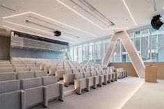 an empty auditorium with rows of chairs and projector screen in the center, overlooking large windows