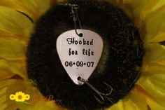 a guitar pick with the words hooked for life on it sitting in front of a sunflower