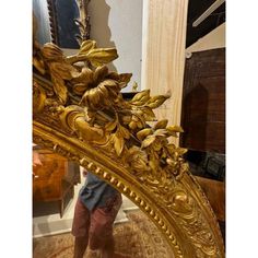 a person standing in front of a mirror with gold leaf designs on the frame and bottom