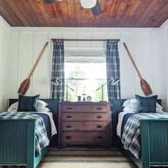 two beds in a room with wooden ceilings and plaid blankets on the bedding, under a ceiling fan