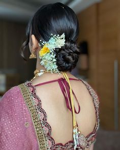 a woman with flowers in her hair wearing a pink sari and gold jewelry on her neck