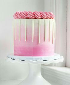 a pink and white cake with icing drizzled on it's side