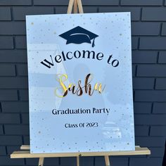 a welcome to sushia graduation party sign hanging on a easel in front of a brick wall