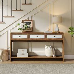 a wooden table with drawers under a stair case next to a lamp and potted plant