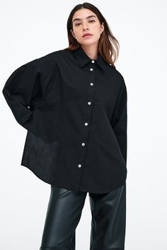 Our Ezra Shirt is a capsule wardrobe dream for your closet. Crafted from 100% crisp European poplin cotton, she offers a classic button-up silhouette in front, but with a cropped back for modern edge. Say hello, as well, to her diagonal seams at the front, sleek collar and long dolman sleeves finished with mother-of-pearl button cuffs. Wear Ezra tucked, tied or open and free—she never fails to inspire new looks.[SPLIT] Rocio, in black and in light blue, is 5'9.5" (175 cm) tall, wearing size XS. Chic Poplin Top With Relaxed Fit, Long Sleeve Poplin Tops With Button Closure, Fall Poplin Button-up Shirt, Fall Workwear Poplin Tops, Chic Poplin Button-up Shirt, Chic Collared Poplin Top, Daywear Poplin Tops With Button Closure, Daywear Tops With Button Closure, Poplin Tops With Button Closure For Daywear