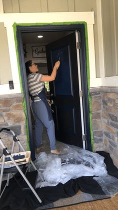 a man is painting the front door of a house with green tape and black paint