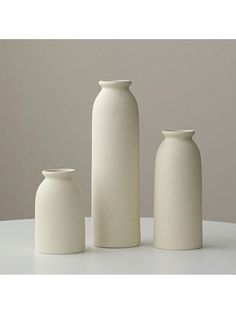 three white vases sitting on top of a table