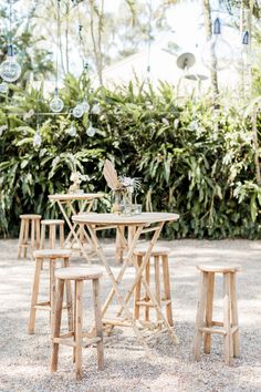 a wooden table and four stools in front of some trees with hanging decorations on them