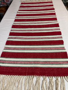 a red and white table runner with fringes on it's end, sitting on a dining room table