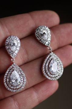 a person holding two pairs of diamond earrings in their hand and the other one is wearing an earring