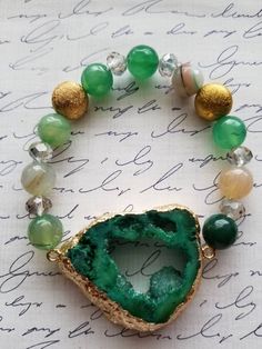 Give your wrist a bold, natural shine with the addition of beautiful crystals! Eclectic in style, this beautiful open green dyed agate pendant offers an irregular shaped druzy cluster with metallic edges of gold foil. The pendant is a great  focal on this bracelet. The druzy is 1.5 inches (1.25 inches in width). The green druzy ia accompanied by green and brown agate rounds, along with facet crystal rondelles. The agate rounds and crystal mixture has swirling patterns and shining facets. The bra Green Bracelets With Natural Stones For Gift, Green Agate Jewelry With Natural Stones, Green Jade Jewelry With Stones, Green Jade Stone Jewelry, Spiritual Green Agate Jewelry, Green Agate Bracelets For Gifts, Green Beaded Stone Bracelets As Gift, Gold Agate Crystal Bracelet For Healing, Green Faceted Spiritual Jewelry