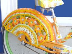 an orange and green bike is decorated with crocheted doily, along with flowers