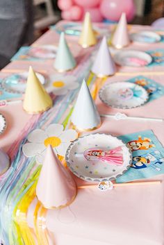 a table topped with paper plates and party hats on top of pink cloth covered tables