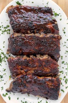 baby back ribs on a white plate with parsley and text overlay that reads oven baked fall off the bone baby back ribs