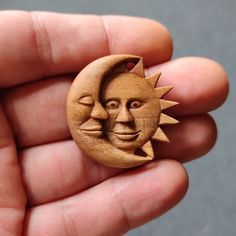 a hand holding a wooden brooch with the face of a sun and moon on it