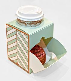 an open box with a cup inside and a donut in the bottom, on a white surface